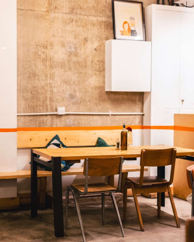 Rudy’s Pizza Napoletana Ancoats interior with wooden tables, open kitchen, and a traditional pizza oven creating a warm, casual dining atmosphere in Manchester.