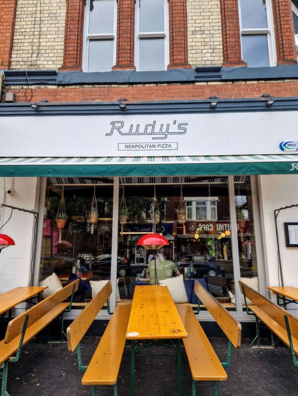 Outdoor seating area at Rudy’s Pizza Chorlton, with wooden tables and chairs set along the pavement