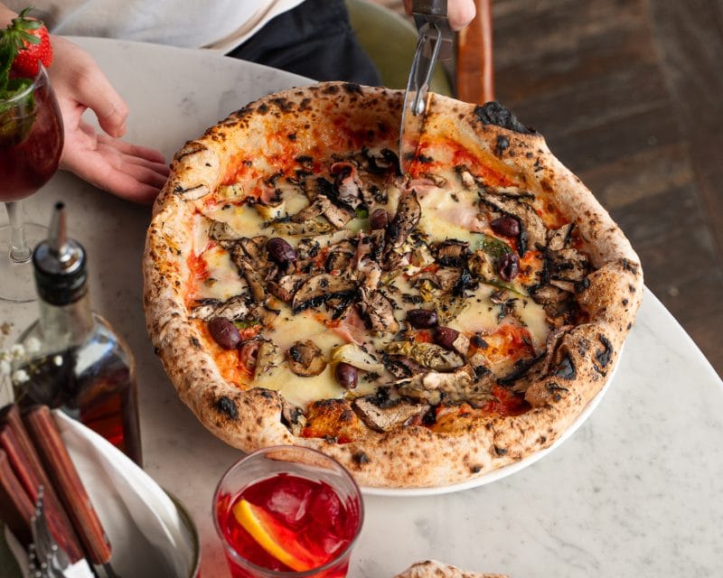 person slicing pizza with cheese and olives