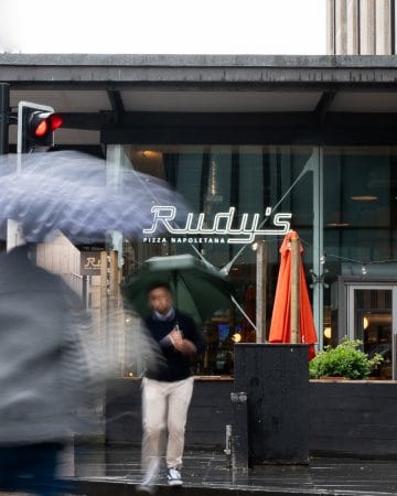 rudy's pizza napoletana location with man standing in front of restaurant with umbrella