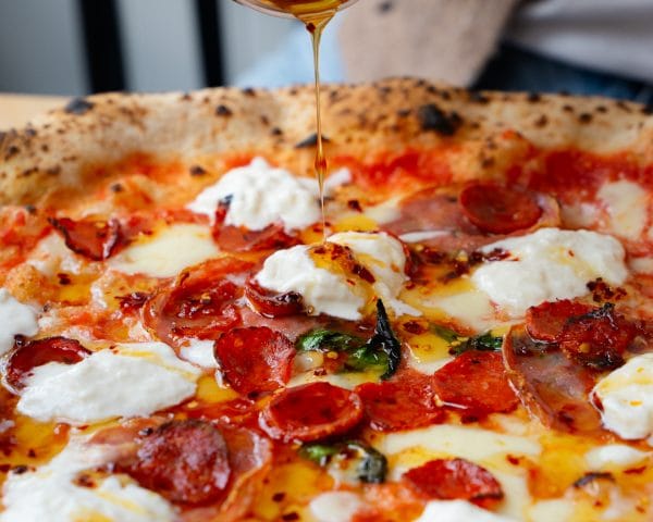 pepperoni and cheese pizza with olive oil being poured