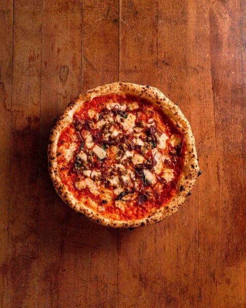 Rudy's Neapolitan pizza topped with tomatoes, cheese, fennel sausage, caramalised onions and chilli flakes