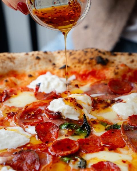 chilli oil being poured over authentic neapolitan pizza