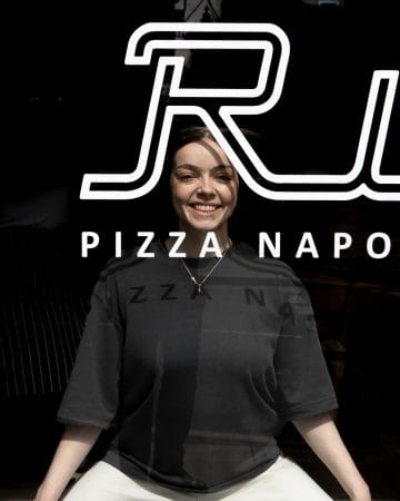 person smiling behind window of rudy's pizza restaurant