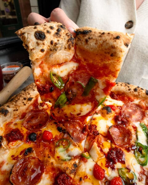 Pizza topped with tomatoes, cheese, salame, roquitto peppers and spicy nduja