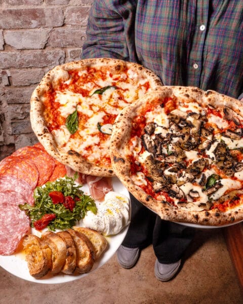 two pizzas topped with tomatoes, mushroom, cheese and a starter with bread, salame, cheese and rocket.