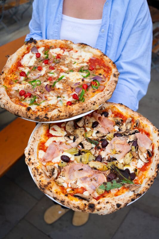 person holding two authentic neapolitan style pizzas